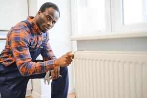 reparar calefacción radiador de cerca. africano hombre reparando radiador con llave inglesa. quitando aire desde el radiador foto