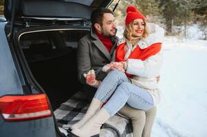 Happy couple sitting in open car back, having stop off. Romantic traveling concept. Winter forest. photo