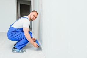 Portrait of a worker in overalls and holding a putty knife in his hands against the plastered wall background. Repair work and construction concept photo