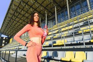 Beautiful girl in sportswear drinks water from a bottle at sunset photo