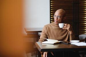 Planning The Day. Calm black student writing his lesson schedule in notebook, sitting in modern bar, empty space. photo