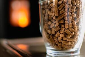 Pellet for stove or boiler in a glass, compressed wood pellet with a stove in background photo