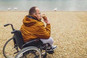 parapléjico minusválido hombre en silla de ruedas es disfrutando al aire libre y Bebiendo café. foto