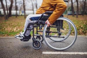 Close up image of paraplegic handicapped man in wheelchair in park. He is rolling on pathway. photo