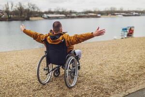posterior ver imagen de parapléjico minusválido hombre en silla de ruedas por el lago. él es disfrutando exterior. foto