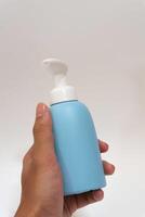 Female hand with blue bottle product for shower on white background. Mockup of unbranded bottle photo