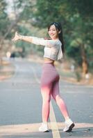 Fitness concept, A cheerful young woman in activewear stretches on a sunny road, with trees lining the pathway. photo
