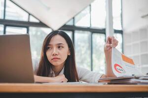 profundo en pensamiento, un joven mujer de negocios planes su trabajo estrategia mientras sentado con su ordenador portátil y notas a un café mesa. foto