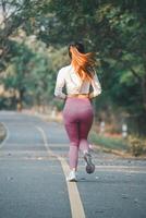 Fitness concept, Rear view of a solitary woman with striking hair jogging on a road lined with trees, early in the morning. photo