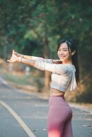 Fitness concept, Fit young woman with a joyful expression stretches on a quiet road, wearing a smartwatch and workout gear. photo