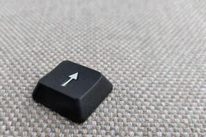 Keyboard with arrow pointing up on grey carpet background, selective focus photo
