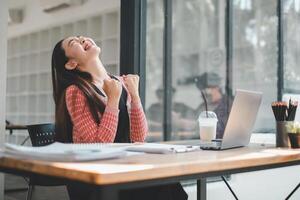 A woman expresses relief and happiness as she takes a break from work, leaning back in her chair with a joyful expression. photo