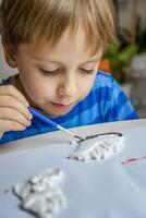 The kid draws and paints plaster figures with a brush and gouache on a piece of paper. photo