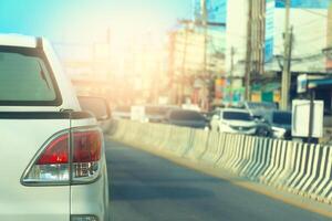 Pickup cars white color driving on the asphalt road at day. Beside with barrier for protect lens. Many car driving on opposite of road with city. photo