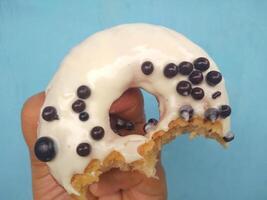 Female hand holds a donut on a blue background. Concept confectionery store, pastries, coffee shop. Banner. Flat lay, top view. photo