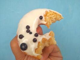 Female hand holds a donut on a blue background. Concept confectionery store, pastries, coffee shop. Banner. Flat lay, top view. photo