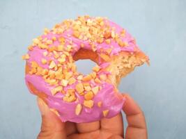 Female hand holds a donut on a blue background. Concept confectionery store, pastries, coffee shop. Banner. Flat lay, top view. photo