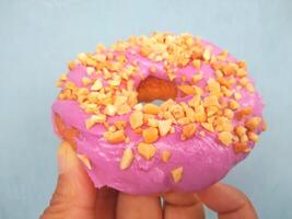 Female hand holds a donut on a blue background. Concept confectionery store, pastries, coffee shop. Banner. Flat lay, top view. photo