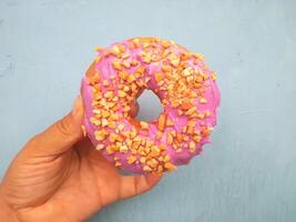 Female hand holds a donut on a blue background. Concept confectionery store, pastries, coffee shop. Banner. Flat lay, top view. photo