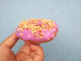 Female hand holds a donut on a blue background. Concept confectionery store, pastries, coffee shop. Banner. Flat lay, top view. photo