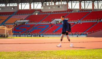 asiático para-atleta relaja y calentar corredor protésico pierna en el pista solo fuera de en un estadio pista paralímpico corriendo concepto. foto