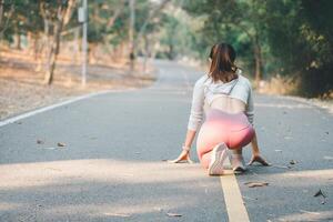 Fitness concept, A woman in fitness attire crouches at the starting position on a park path, preparing for a morning run. photo