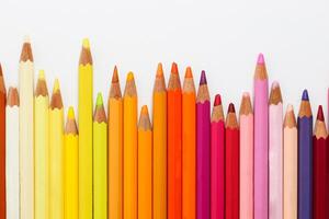 Multi-colored pencils lie on a white table, the red range of colors photo