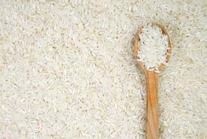 White long rice in a wooden spoon on a rice background. Banner. Top view. Close-up. Selective focus. photo