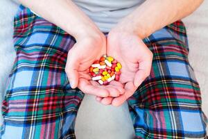 Man holds many multicolored pills in hands. Taking vitamins, supplements, antibiotic, antidepressant and painkiller medication. Close-up. photo