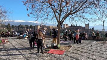 Granada, Spanien - - 21 Februar 2024- Menschen und Touristen gehen durch das san nicolas Standpunkt und nehmen Fotografien, beobachten das Alhambra und Sierra Nevada im das Hintergrund. video