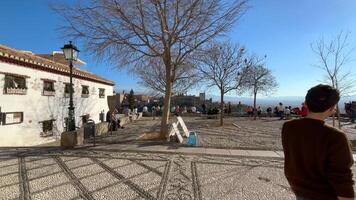 Granada, Spanien - - 21 Februar 2024- Menschen und Touristen gehen durch das san nicolas Standpunkt und nehmen Fotografien, beobachten das Alhambra und Sierra Nevada im das Hintergrund. video