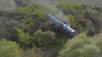 aéreo Visão do uma trem viajando sobre uma estrada de ferro ponte sobre uma rio. zangão voar sobre a locomotiva e carruagens do a limitar calibre estrada de ferro. video