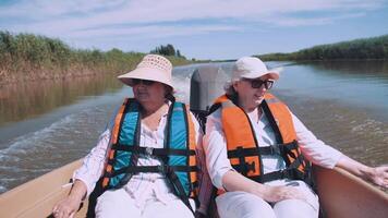 deux content femelle touristes toucher le l'eau de une bateau tandis que en voyageant sur le rivière. femmes jouer avec l'eau gouttes. des moments de tourisme. la vie est merveilleux. personnes âgées tourisme. video