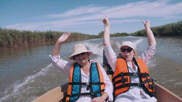 dois feliz fêmea turistas toque a água a partir de uma barco enquanto viajando em a rio. mulheres jogar com água gotas. momentos do turismo. vida é maravilhoso. idosos turismo. video
