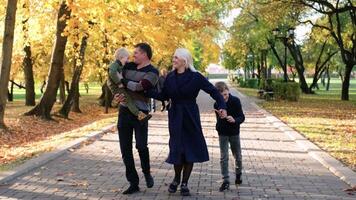 een familie van vier wandelen in de herfst park, hebben pret en voor de gek houden in de omgeving van. horizontaal langzaam beweging video