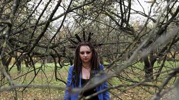 Portrait of a Woman in a blue leather jacket with dreadlocks and a headband with feathers. Woman posing in autumn park and looking at camera. Horizontal slow motion video