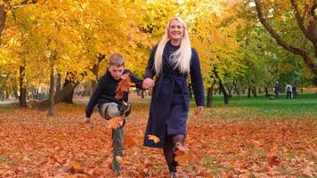 Mutter und Sohn sind Gehen im das Park, halten Hände und werfen Herbst Blätter oben mit ihr Füße. horizontal schleppend Bewegung Video