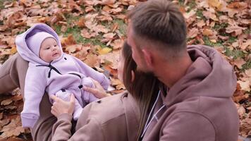 Jeune Parents sur une marcher avec leur nouveau née fille dans le l'automne parc. mère et père asseoir sur une couverture, une nouveau née fille mensonges sur sa de la mère tour video