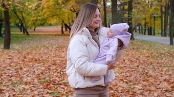 Young mother with newborn baby in autumn park. Mother shakes the child in her arms so that the girl does not cry. video