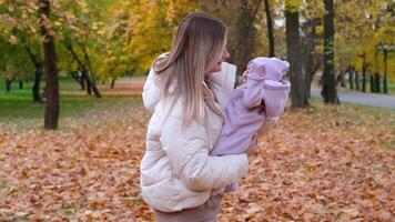 Young mother with newborn baby in autumn park. Mother shakes the child in her arms so that the girl does not cry. video