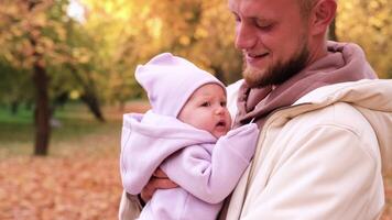 A young father with a newborn daughter in the autumn park. The father shakes the girl in his arms so that she does not cry video