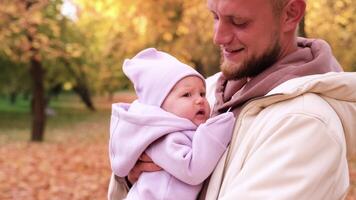 une Jeune père avec une nouveau née fille dans le l'automne parc. le père secoue le fille dans le sien bras donc cette elle Est-ce que ne pas cri video