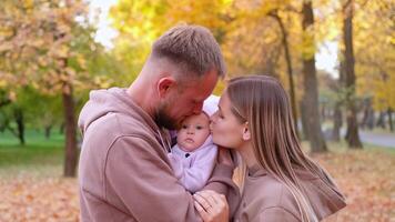 joven madre y padre son caminando con un recién nacido bebé en el otoño parque. padres besos su recién nacido hija video