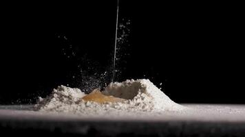 Chicken egg falls in slow motion into flour on black isolated background close up in 4K video