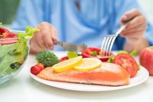 Asian elderly woman patient eating salmon steak breakfast with vegetable healthy food in hospital. photo