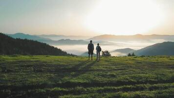 två turister på de topp av de berg tittar på de soluppgång och de Fantastisk landskap i de bergen och de dimma liggande i de dal mellan de berg. natur och skönhet av en morgon- turist video