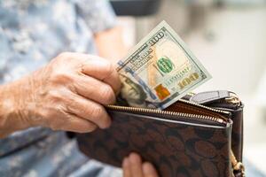 Asian senior woman holding and counting US dollar banknotes money in purse. Poverty, saving problem in retirement. photo