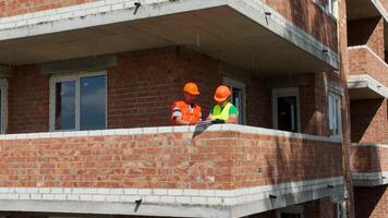 Construction of a house. Engineers and architects review the construction plan. Two engineers wearing safety helmets are having a discussion on a construction site. video