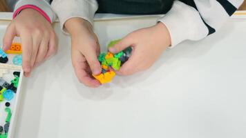 une enfant pièces avec une lego constructeur. fermer de une les filles mains assemblage une lego video