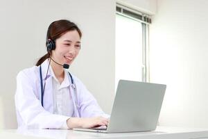 Asian female doctor smiling beautifully Providing treatment services for patients with online conversations via the Internet on laptop computers. online doctor concept. Copy space photo